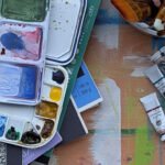 Learn to draw before you paint. Flat lay of expensive beginner art mistakes including Arches watercolor blocks, QoR and Da Vinci paint tubes, and a messy palette. Line & Blossom Design